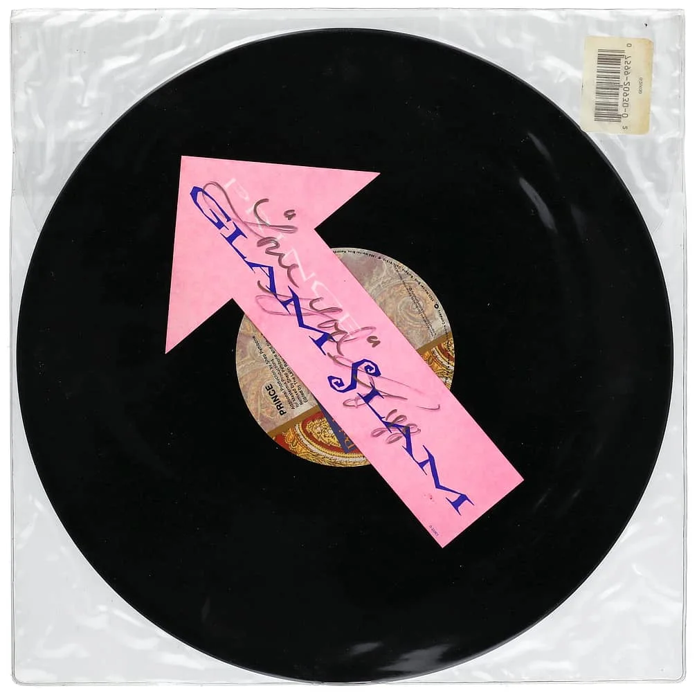 A vinyl record in a transparent sleeve, featuring a design with a large pink arrow and the text "Slaves of New York" on the arrow.