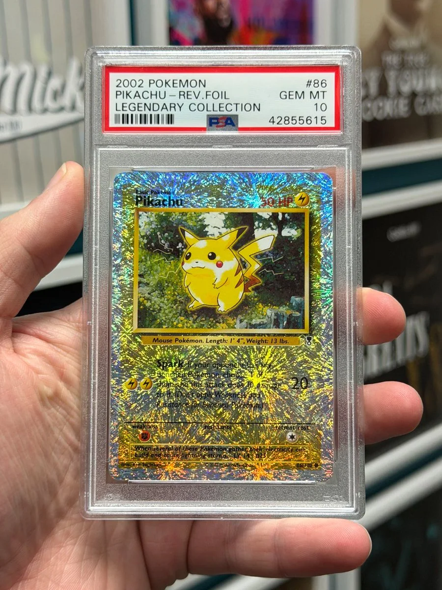 A hand holds a graded 2002 Pokémon card featuring Pikachu. The card has a reflective foil background.