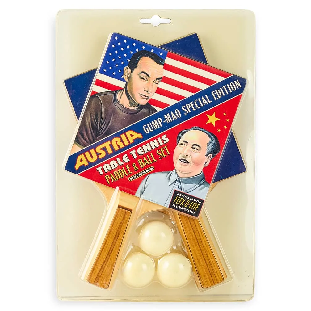 Packaging for a table tennis paddle and ball set labeled "Austria Gump-Mao Special Edition" featuring illustrations of two individuals. One paddle displays an illustration with a U.S. flag, while the other has a Chinese flag. Three balls are included.
