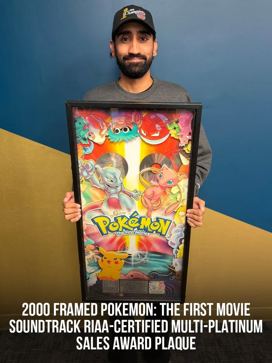 A person is holding a framed Pokémon: The First Movie soundtrack plaque, signifying RIAA-certified multi-platinum sales. The background has a geometric design with blue and gold colors, and the person is wearing a cap.