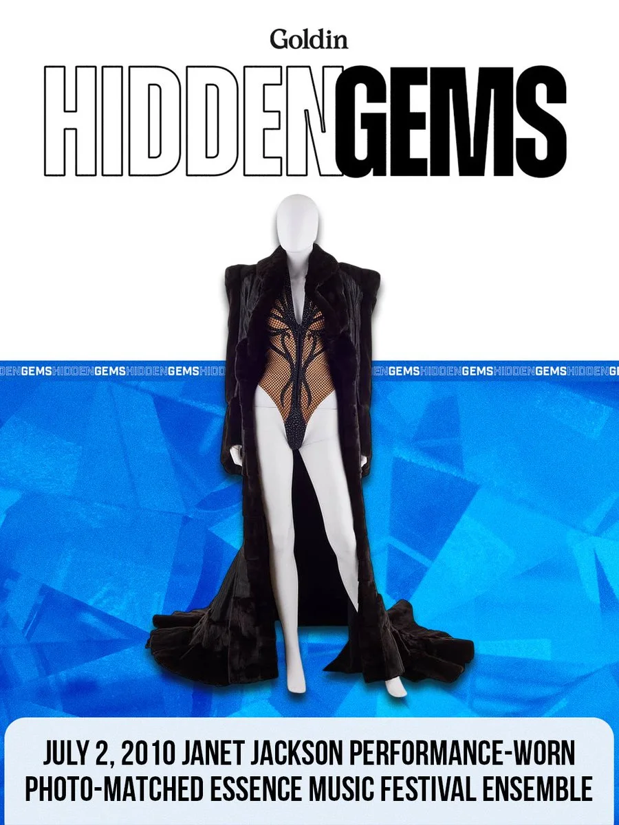 A mannequin displays an intricate costume with a sheer bodysuit and a flowing, dark coat. The text above reads "Goldin Hidden Gems," and below, it notes the outfit as "July 2, 2010 Janet Jackson Performance-Worn Photo-Matched Essence Music Festival Ensemble.