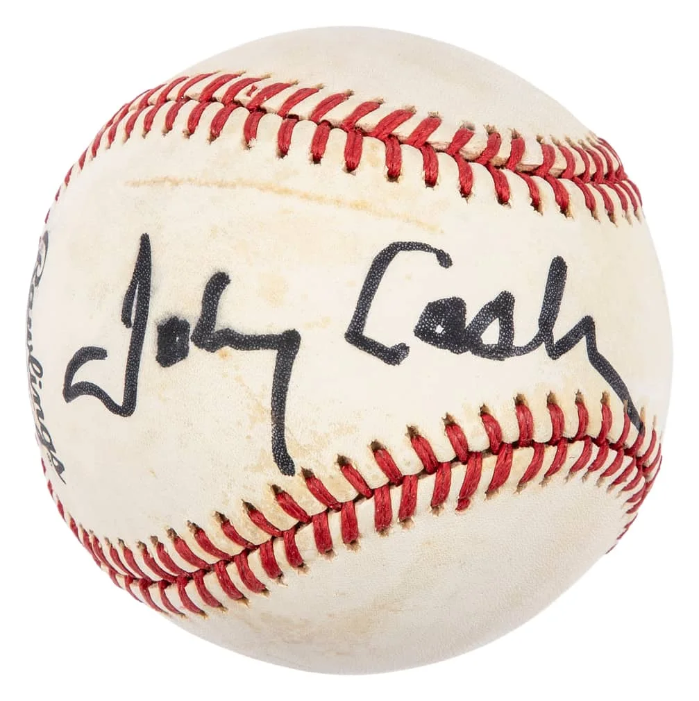 A baseball signed with the name "Johnny Cash" in black ink, featuring red stitching and the Rawlings logo partially visible.