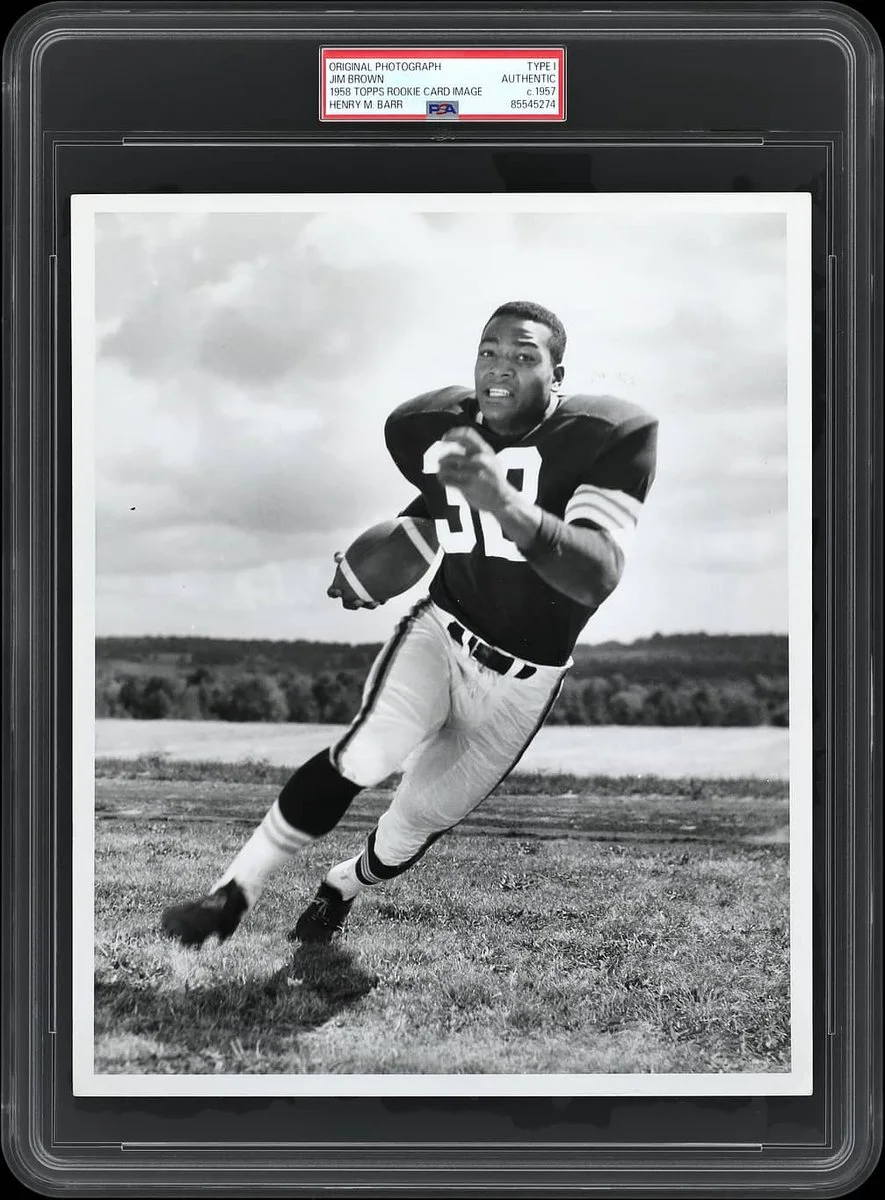 A person in a football uniform is running on a grass field, holding a football. The uniform features the number 39. The image is in black and white and is encased in a collectible frame marked "Henry B. Iba." The sky is partly cloudy in the background.