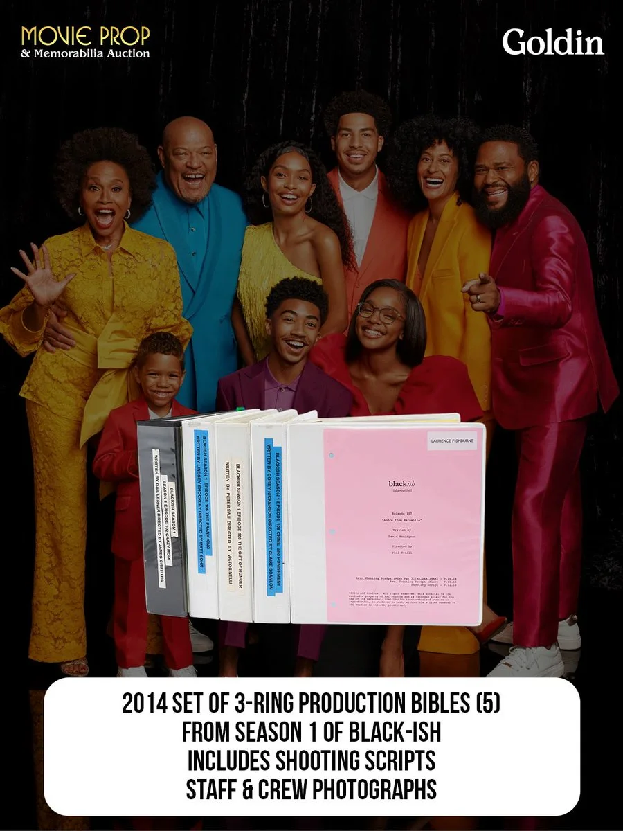 A group of people are standing together, smiling warmly at the camera. They are dressed in vibrant and elegant attire. In front of them is a display of a 2014 set of 3-ring production bibles from Season 1 of "Black-ish," which includes shooting scripts, staff, and crew photographs. The image mentions "Movie Prop & Memorabilia Auction" and "Goldin.