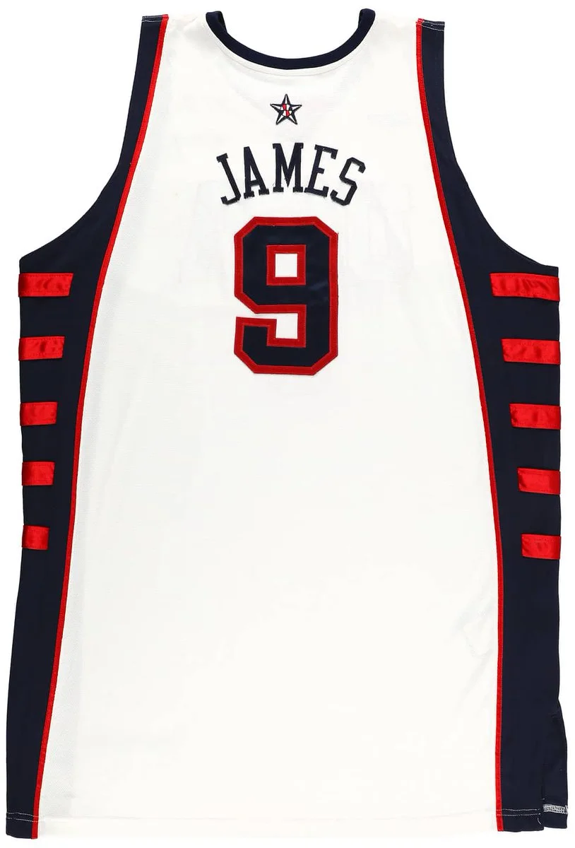 A basketball jersey featuring the name "James" and the number 9. The jersey is predominantly white with dark side panels and red accents. An embroidered star is located at the top.
