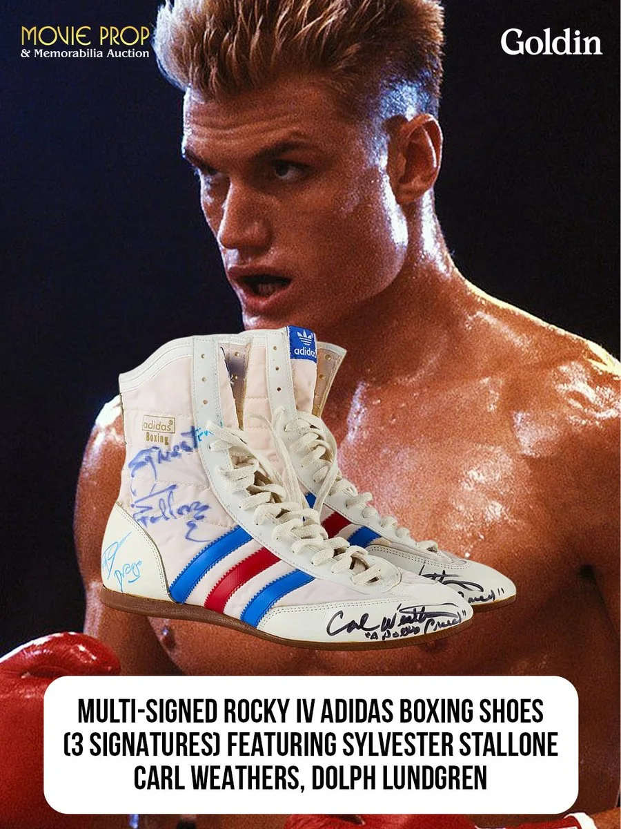 This image features a person in a boxing pose, with sweat visible on their skin, set against a dark background. In the foreground are a pair of multi-signed Adidas boxing shoes with red, white, and blue stripes. The shoes include signatures from Sylvester Stallone, Carl Weathers, and Dolph Lundgren. Text on the image advertises a movie prop and memorabilia auction by Goldin.