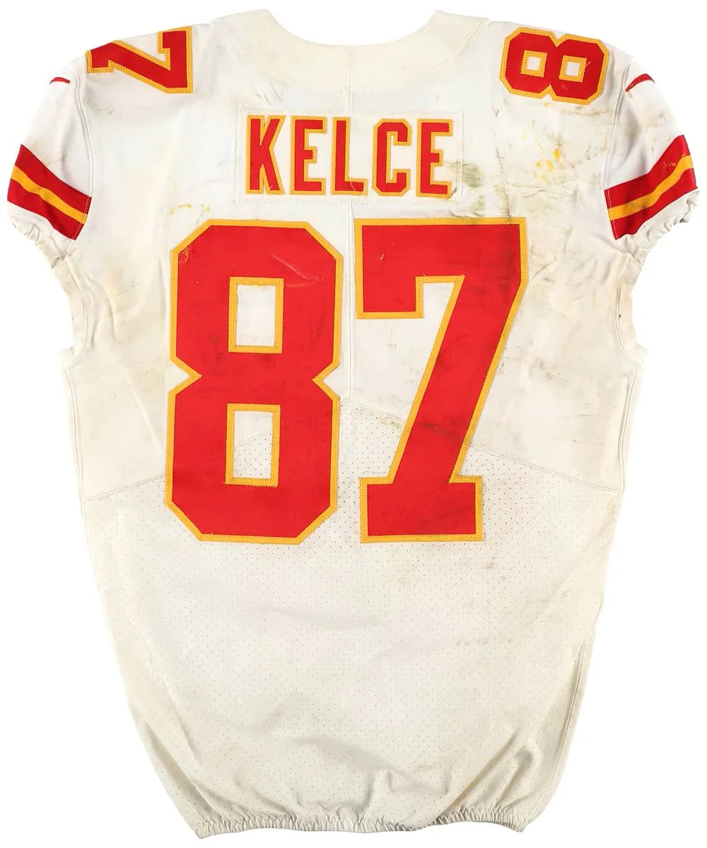 The image shows a Kansas City Chiefs football jersey with the number 87 and the name "Kelce" on the back. The jersey is white with red and yellow accents and appears to be stained.