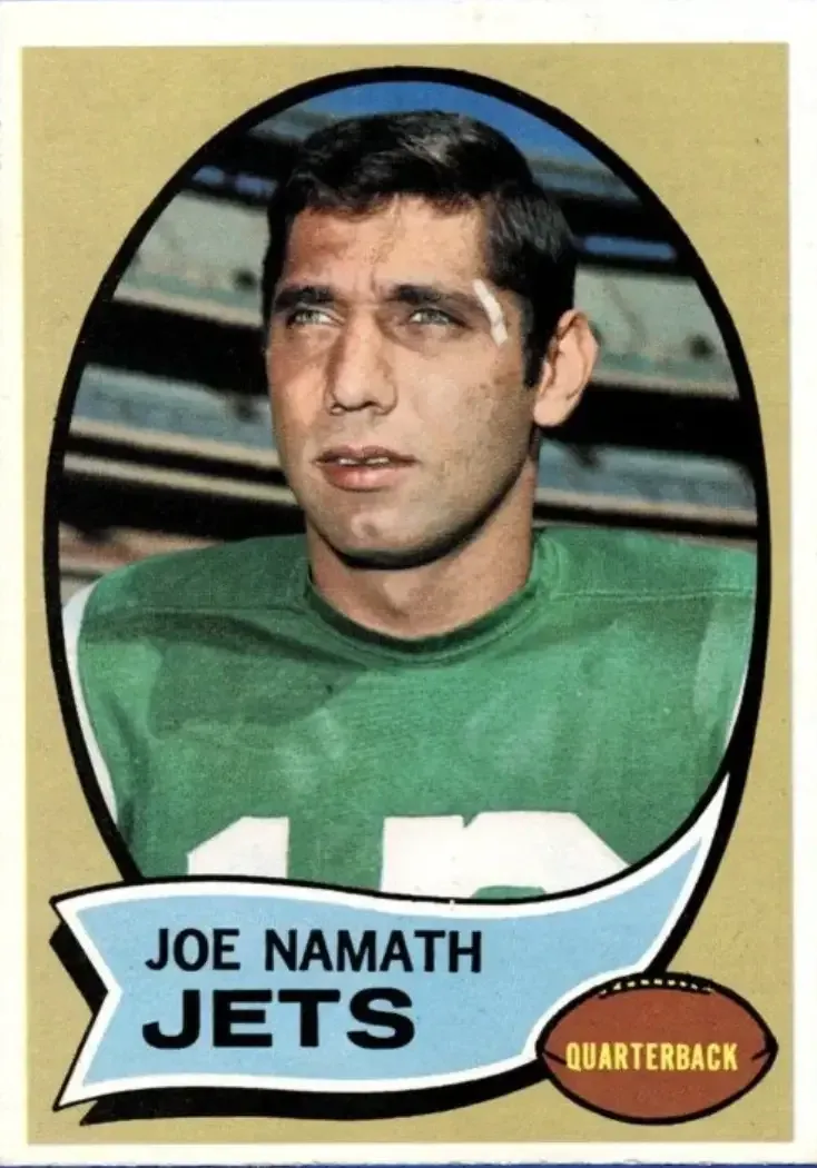 Image of player on sidelines in green jersey with stadium stands behind him.
